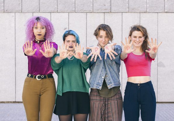 group of young and diversity women with the symbol of feminism written oh their hands and showing them to the front